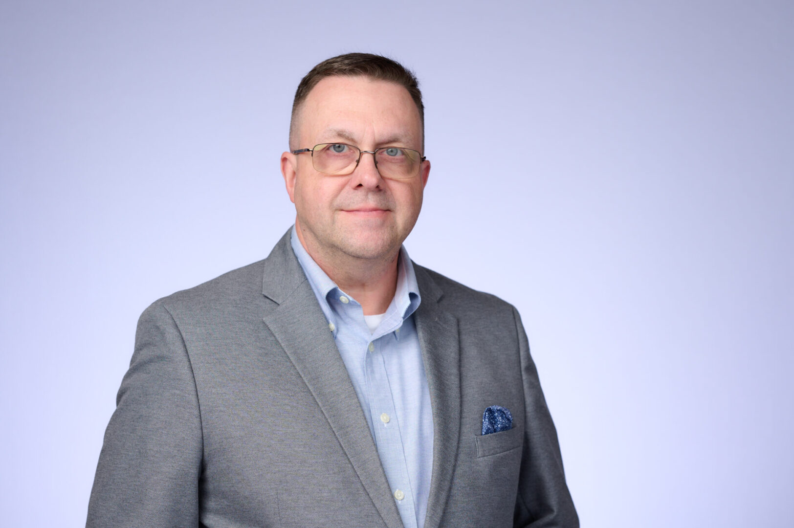 Professional man in glasses wearing a gray blazer and blue shirt.